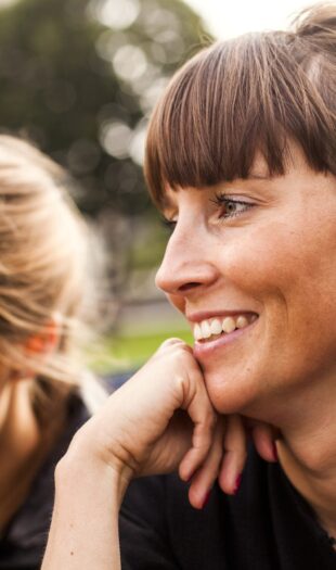 Happy woman sitting with female friend at park Happy woman sitting with female friend at park